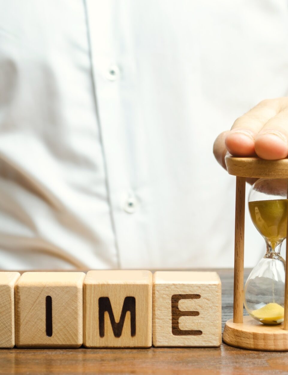 A man puts hourglass near wooden blocks with the word Time