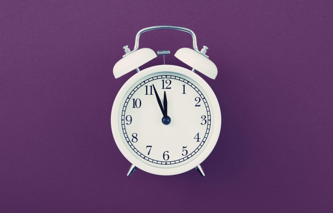Alarm clock showing five minutes to twelve on purple background Alarm clock showing five minutes to twelve on purple background