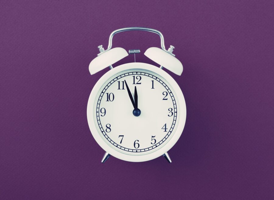 Alarm clock showing five minutes to twelve on purple background