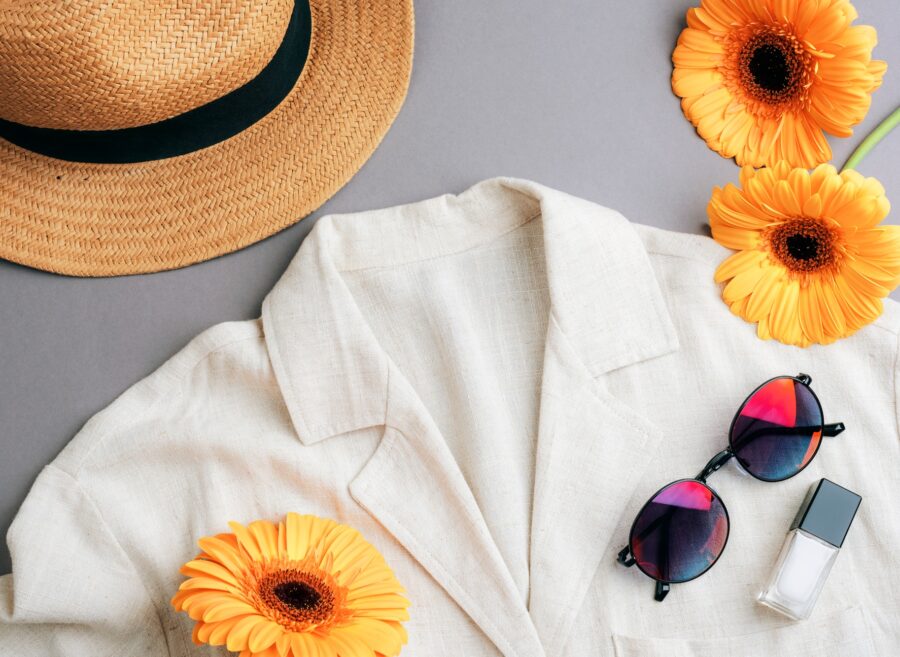 Woman's fashionable accessories: linen blouse, straw hat, eyeglasses, nail polish and orange gerbera